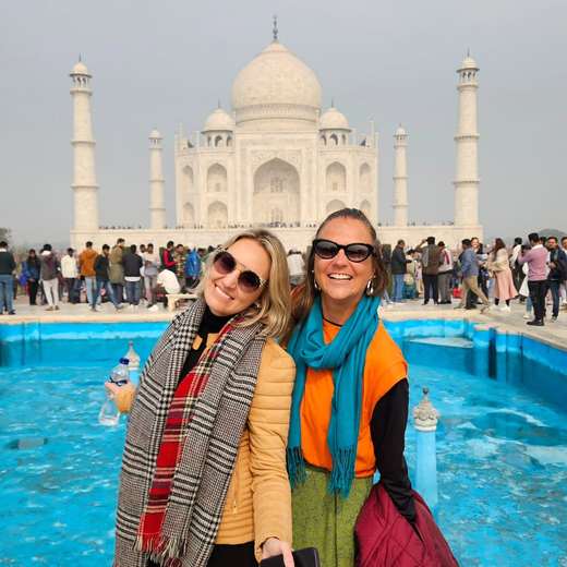 Duas amigas de cachecol sorrindo diante do Taj Mahal, na Índia
